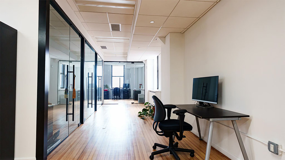 Hallway with glassfront conference rooms and one desk